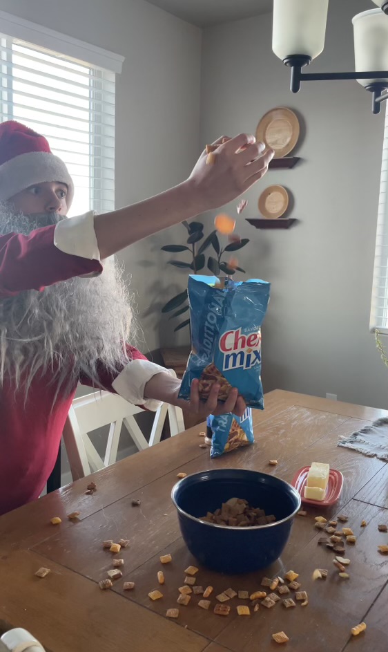 Landon Payne in a santa costume putting Chex Mix(TM) into the bag at a dining table.