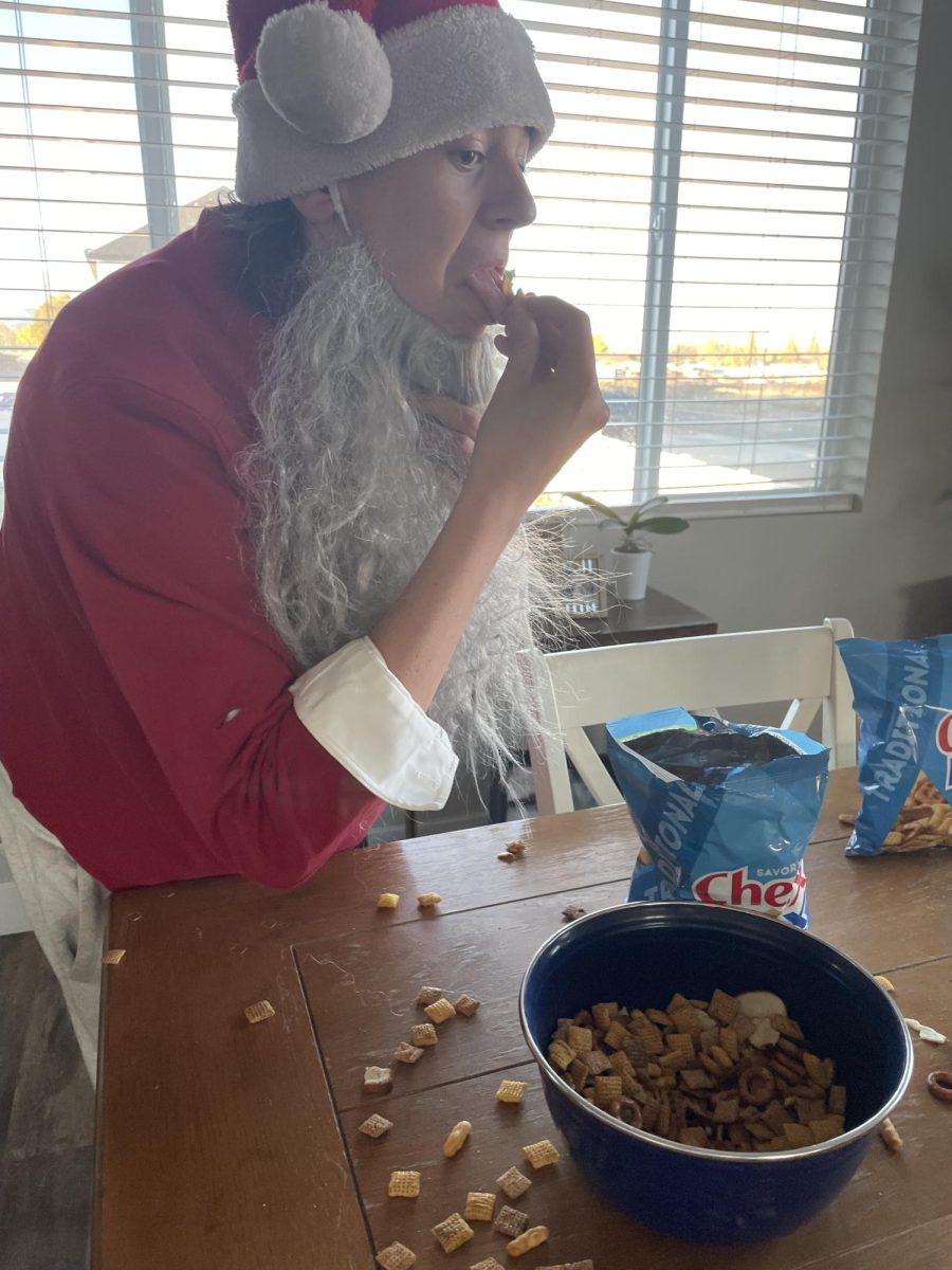 Landon Payne in a santa costume pulling his fake beard down to eat Chex Mix(TM)
