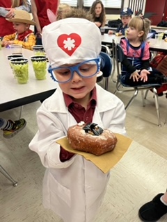 Little Preschooler in is doctor costume showing off his spooky doughnut 